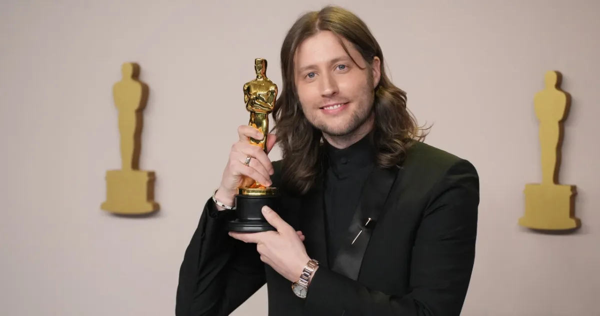 Ludwig Goransson holds his Academy Award close to his face on the Oscars red carpet.