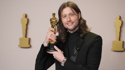 Ludwig Goransson holds his Academy Award close to his face on the Oscars red carpet.