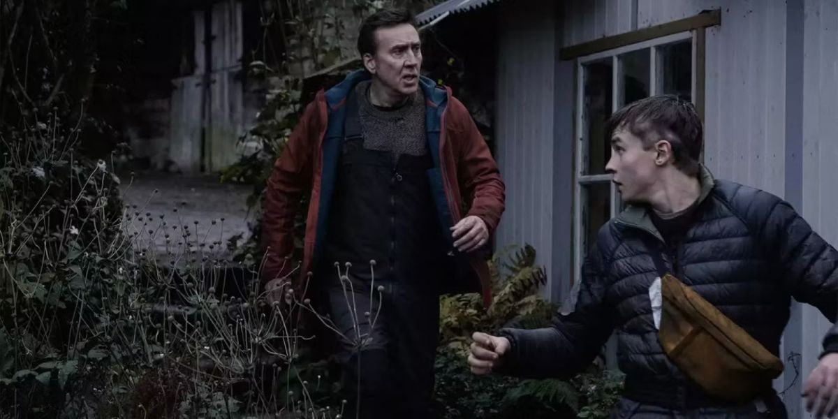 Nicolas Cage and Maxwell Jenkins walk past a farmhouse in a dark, blue toned lit image