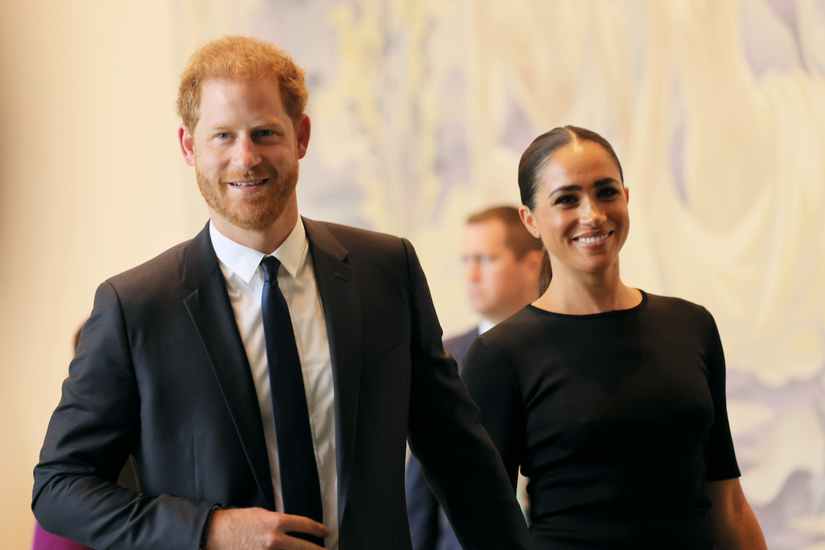 Prince Harry and Meghan Markle walk holding hands and smiling.