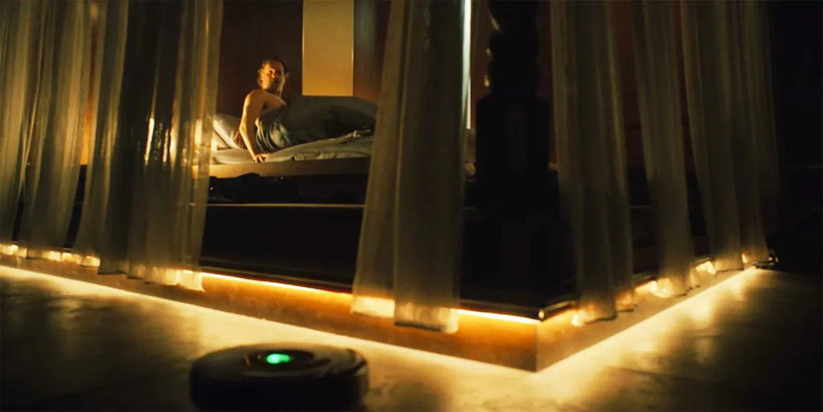 Andrew Lincoln in bed staring at a Roomba