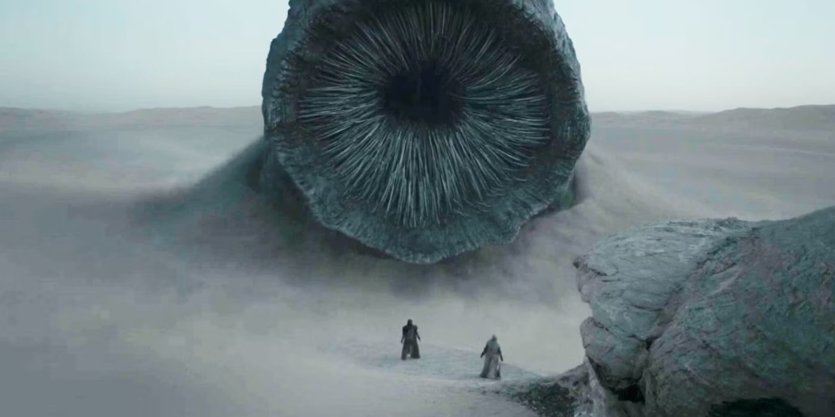 A sandworm looms over two tiny figures standing in front of it.