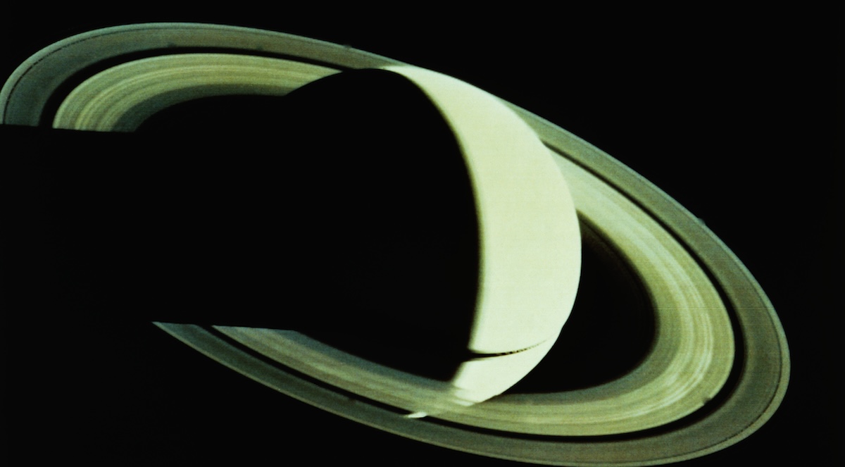 The planet Saturn, partially cloaked in shadow.