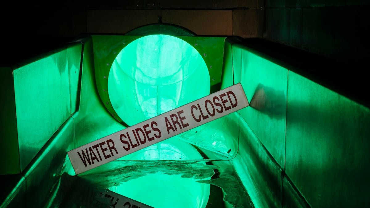 Sign at the bottom of a water slide saying it is closed in an abandoned swimming pool