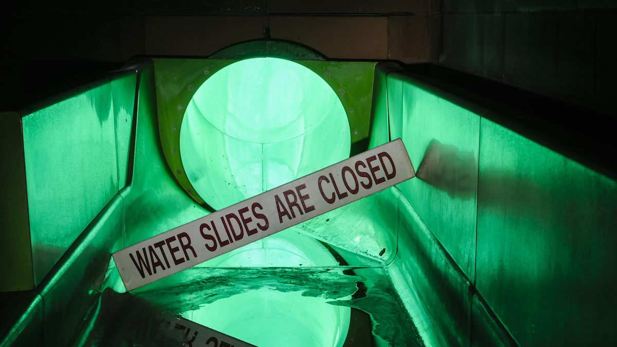 Sign at the bottom of a water slide saying it is closed in an abandoned swimming pool