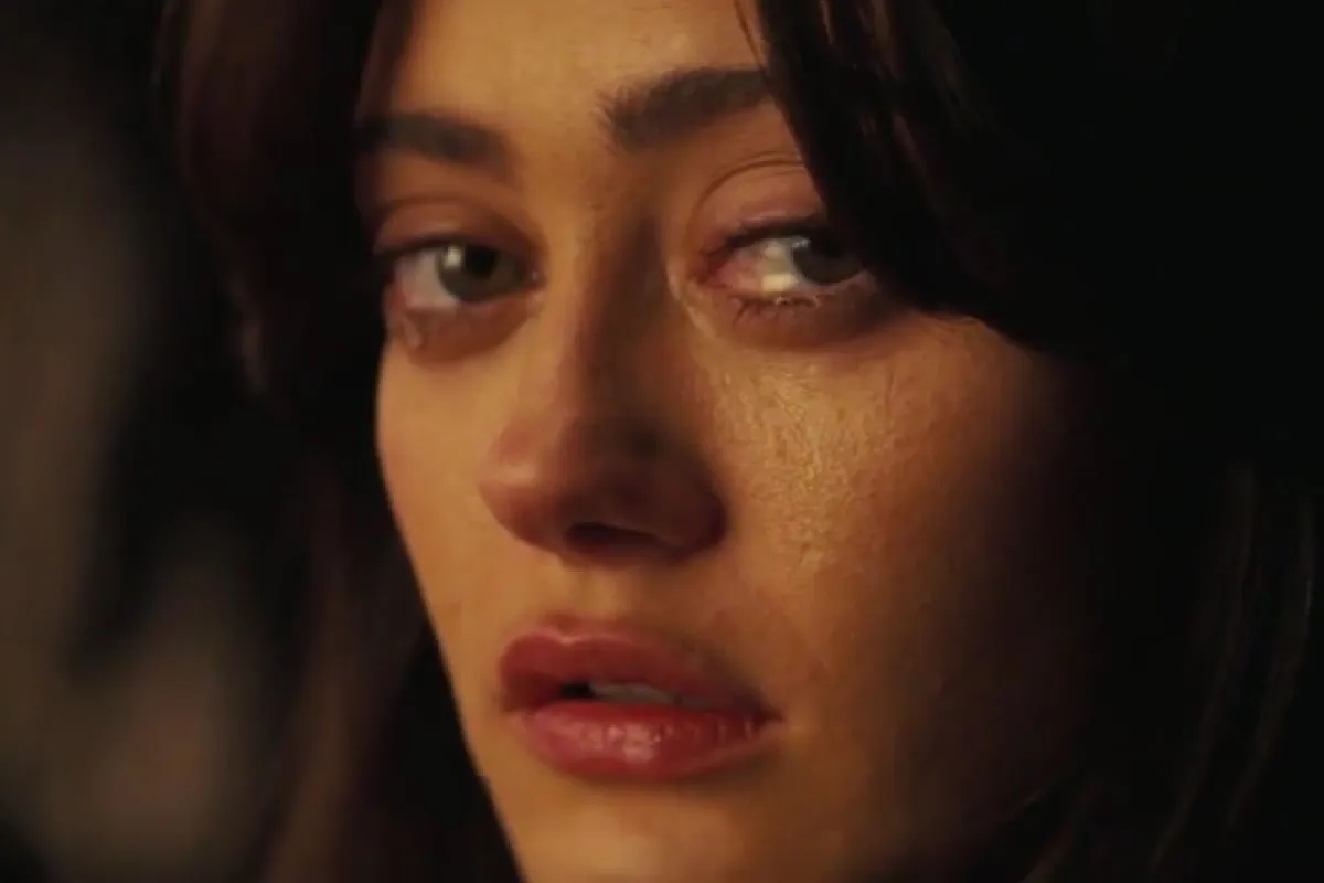 Close-up of Ella Purnell as Lucy in Prime Video's 'Fallout.' She is a white woman with long dark hair. Her face is turned to the side to look at the camera, and she is angry and disillusioned with tears in her eyes.
