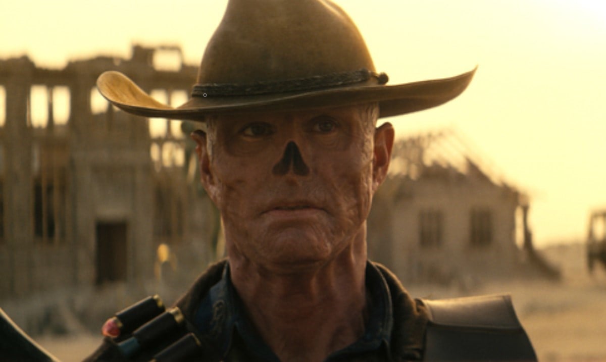 Image of Walton Goggins as The Ghoul in Prime Video's 'Fallout.' He is a man who has been irradiated to the point of his skin being red and wrinkly, having no hair, and no nose. He's wearing a cowboy hat and strapped with weapons as he walks through the Wasteland.