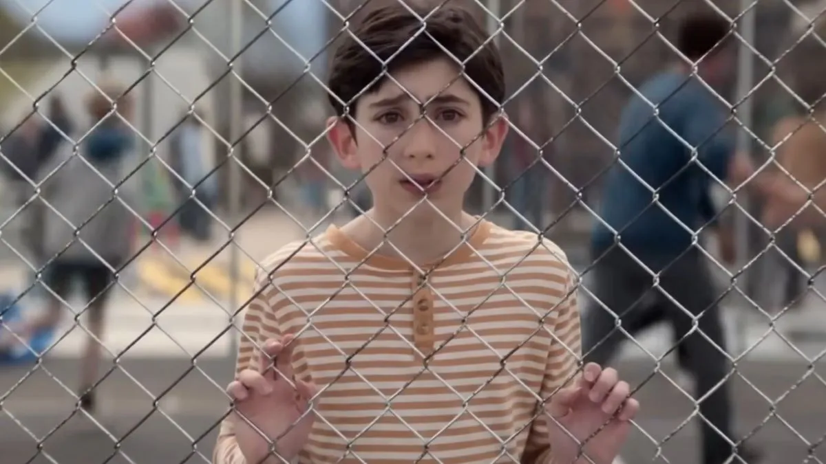 little boy looking scared through a chain link fence