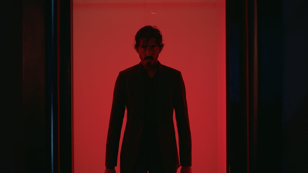 Dev Patel standing in a red hallway in a black silhouette 
