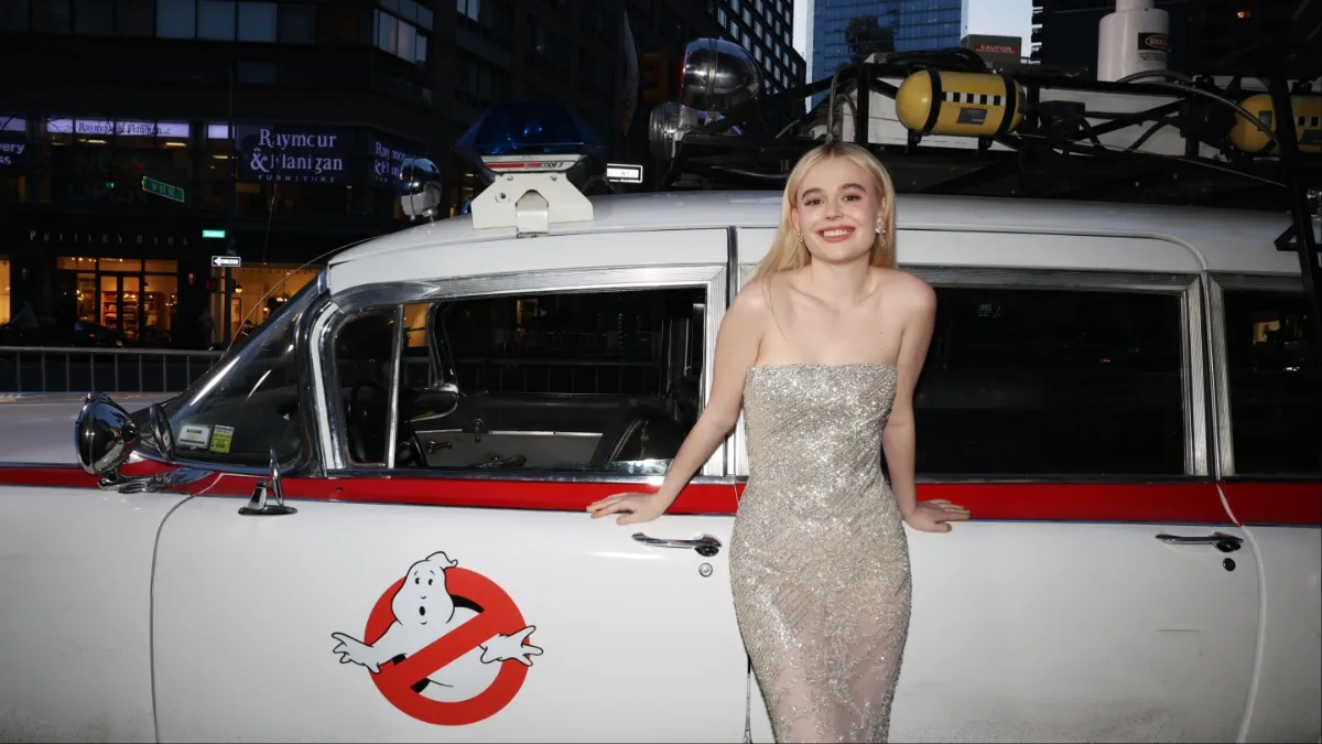 Emily Alyn Lind poses in front of the ECTO-1 at the 'Ghostbusters: Frozen Empire' premiere.