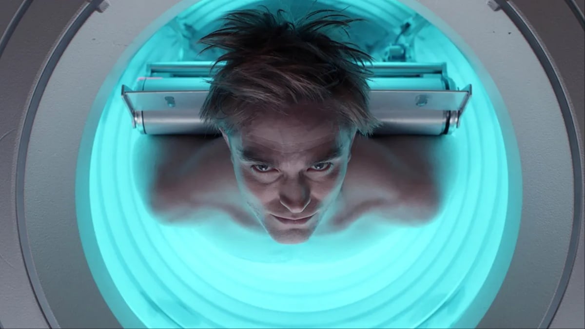Robert Pattinson emerges from a blue-lit machine cylinder in 'Mickey 17'.