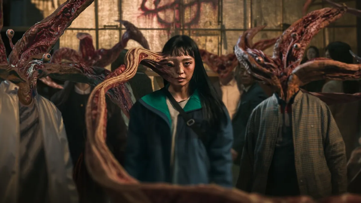 A woman with a tentacle coming out of her head stands in front of alien/human hybrids in "Parasyte: The Grey" 