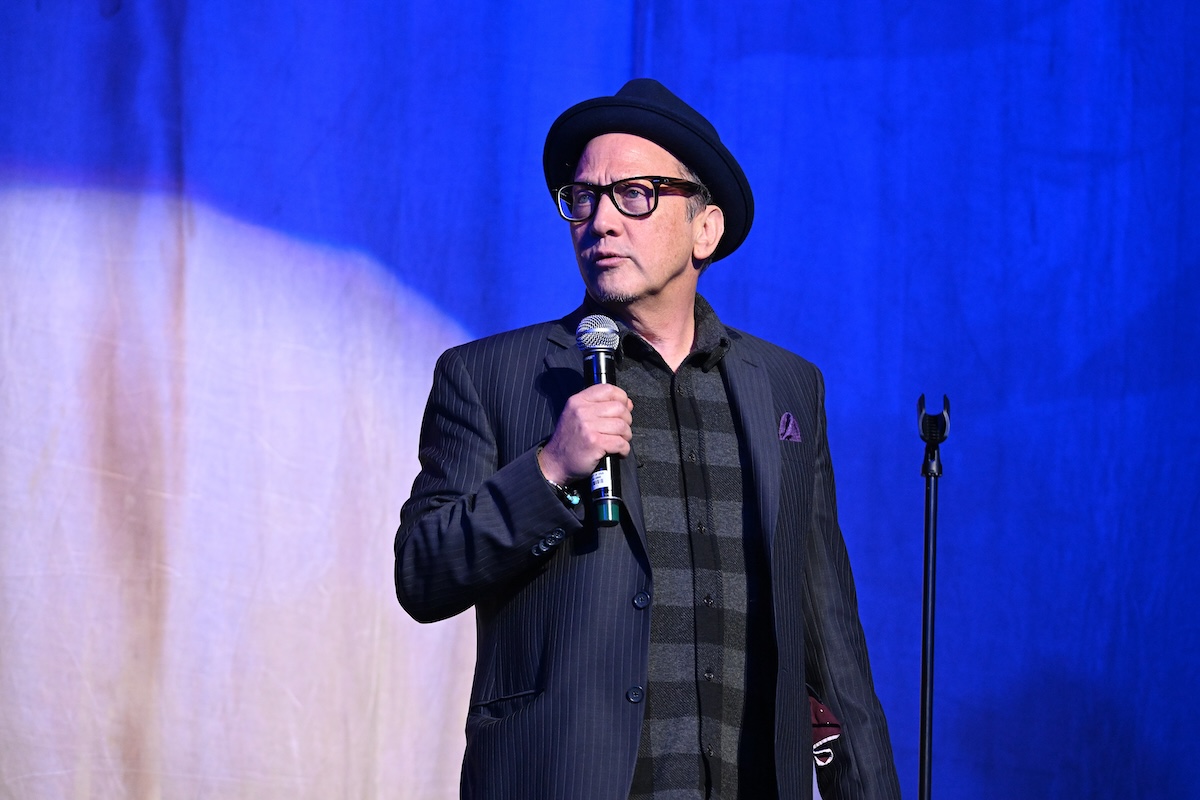 Rob Schneider standing with a microphone in his hand on stage