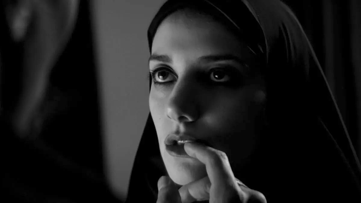 The vampire girl about to bite off a man's finger in "A girl walks home alone at night"