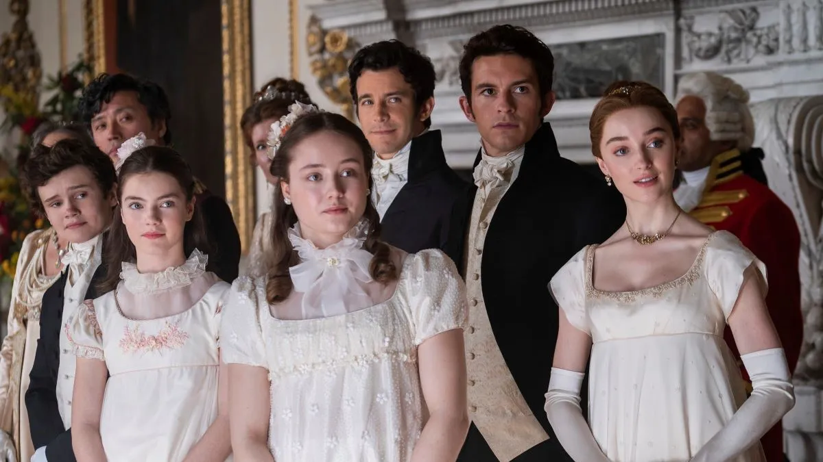 Image of several of the Bridgerton siblings on the Netflix series, 'Bridgerton.' Six of them, three of the girls and three of the boys, are standing at a party all looking in the same direction at something.