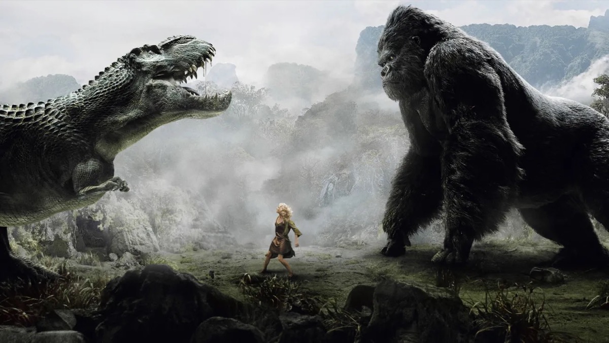 A giant ape faces off against a T-Rex while a woman stands trapped in between