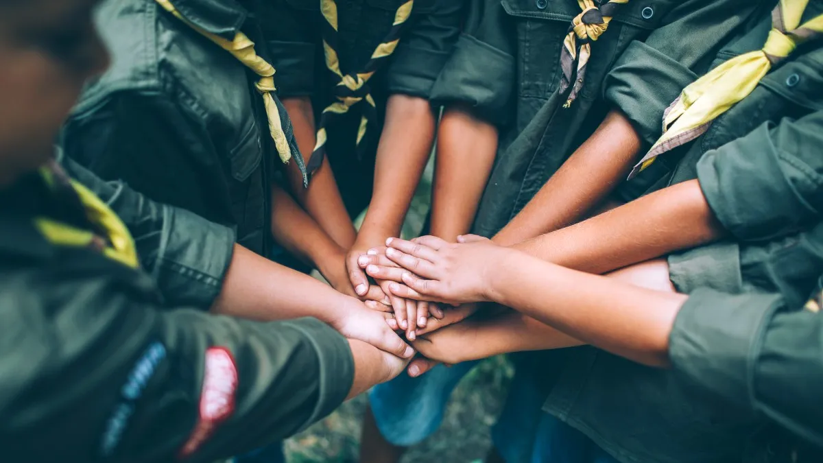 A group of young scouts stack their hands in a circle
