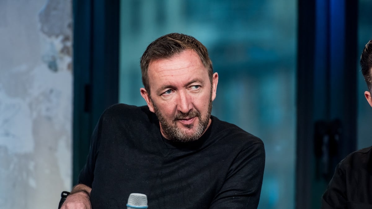 Ralph Ineson holds a microphone on a stage.