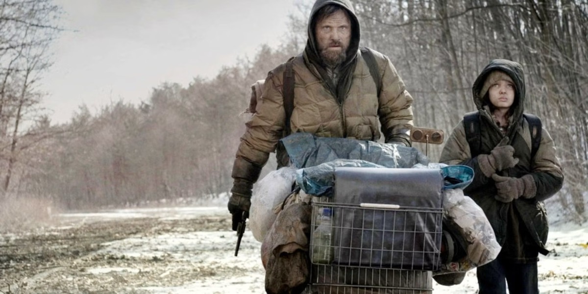 A father and son push a shopping cart down a desolate road in "The Road" 