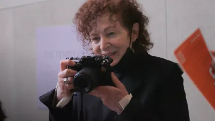 A woman in a mask holds a camera in 