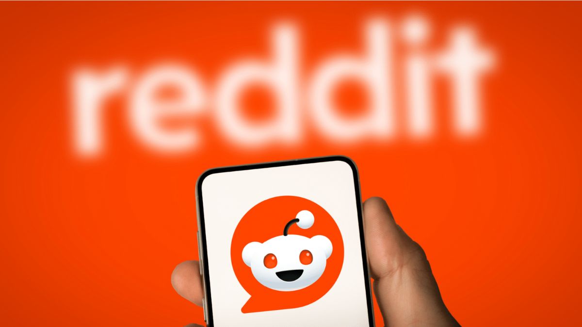 A picture of a smartphone with the Reddit logo man on the screen, in front of an orange background.
