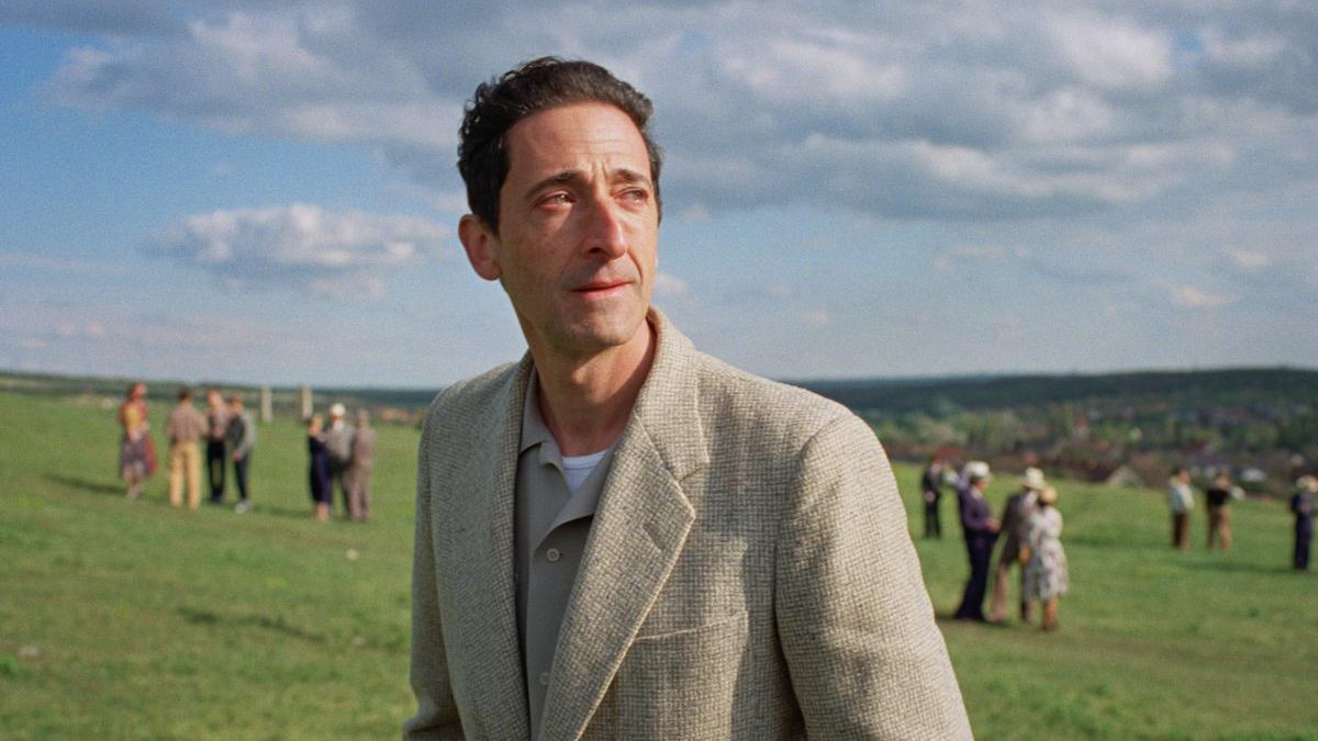 Adrien Brody standing in a field in The Brutalist