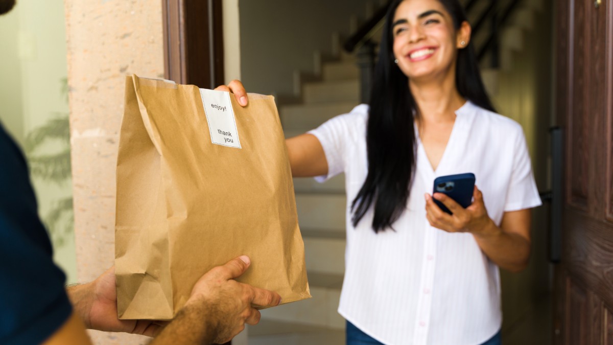 A woman accepts a takeout bag from a food delivery worker