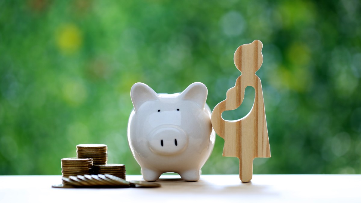 Wooden silhouette of a pregnant woman next to a piggy bank and coins
