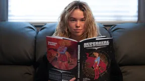 milly alcock holding a comicbook and looking up
