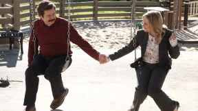 leslie and ron holding hands on swings