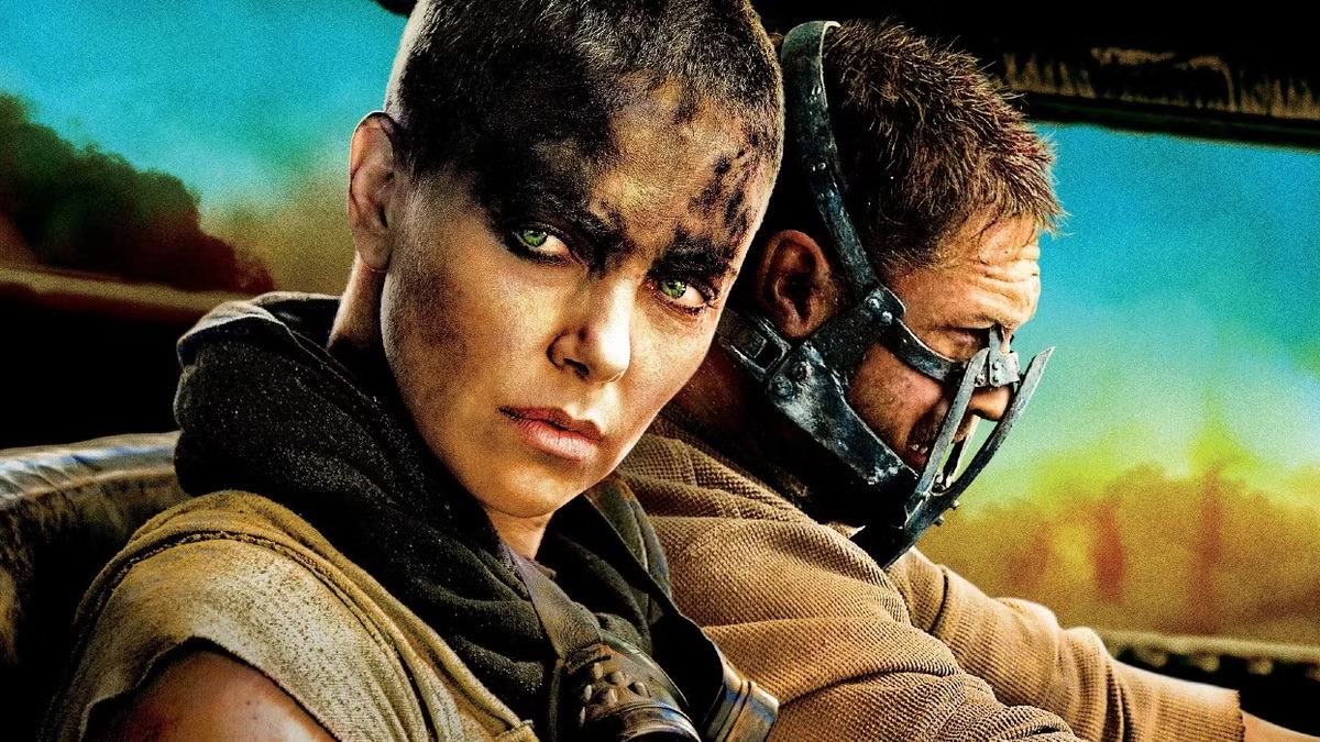 A woman with oil on her face looks out a car window while a man drives in "Mad Max: Fury Road"