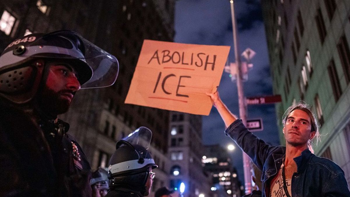 NEW YORK, NEW YORK - OCTOBER 21: A person holds a sign reading "Abolish ICE" as NYPD Strategic Response Group officers keep watch over people protesting against an earlier raid by federal agents outside of 26 Federal Plaza on October 21, 2025 in New York City. (Photo by Adam Gray/Getty Images)