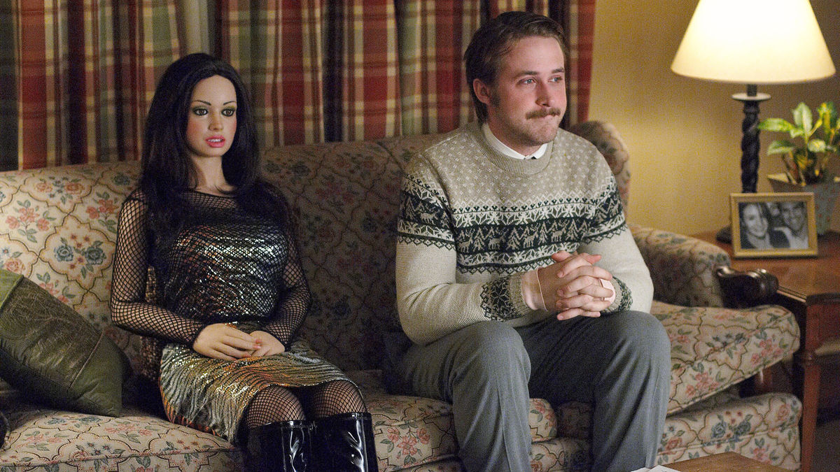 A sweet looking man sits on the couch with a lifelike plastic doll in "Lars And The Real Girl"