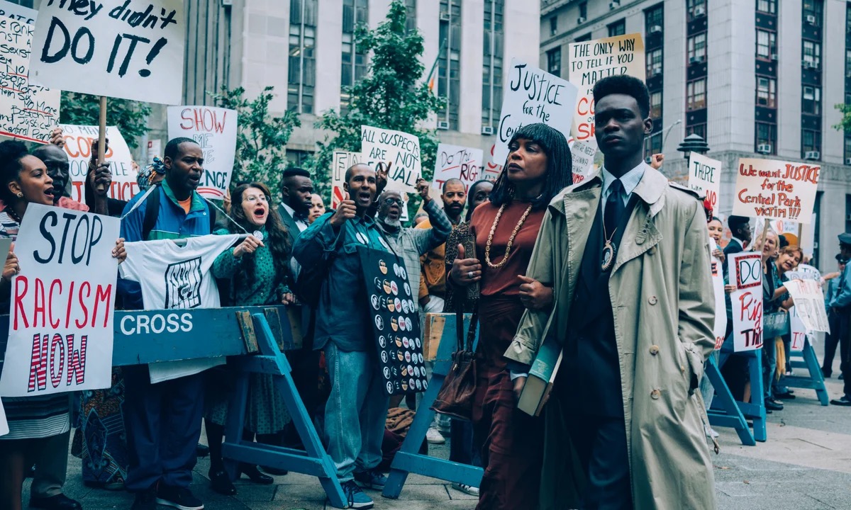 A young man walks somberly past a group of protestors in "When They See Us" 