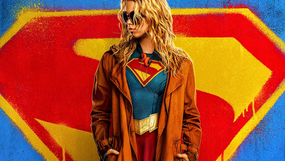 Kara Zor-El standing in front of a logo