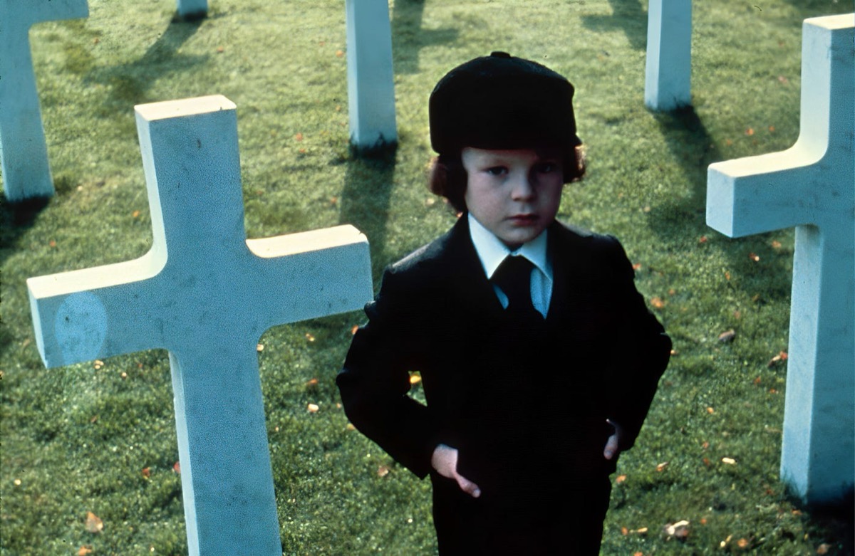 A little boy stands in front of cross gravestones in "The Omen" 