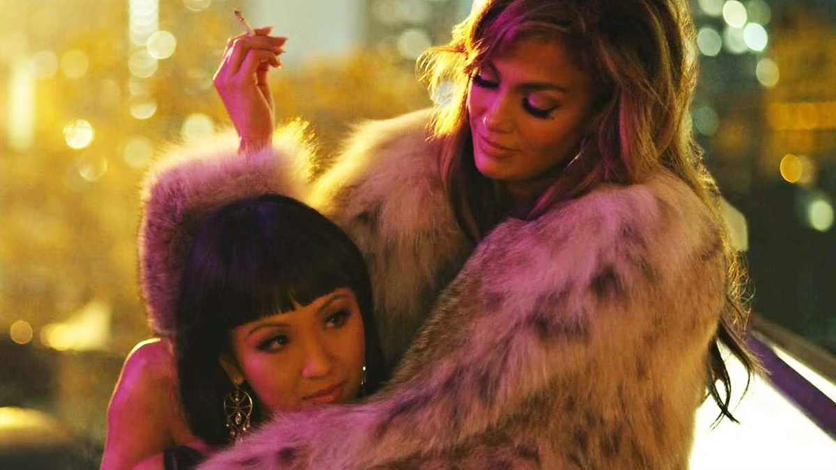 A stripper in a fur coat wraps her arms around another in "Hustlers" 