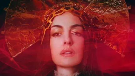 A pop star in a relgious headpiece stands in red light in 