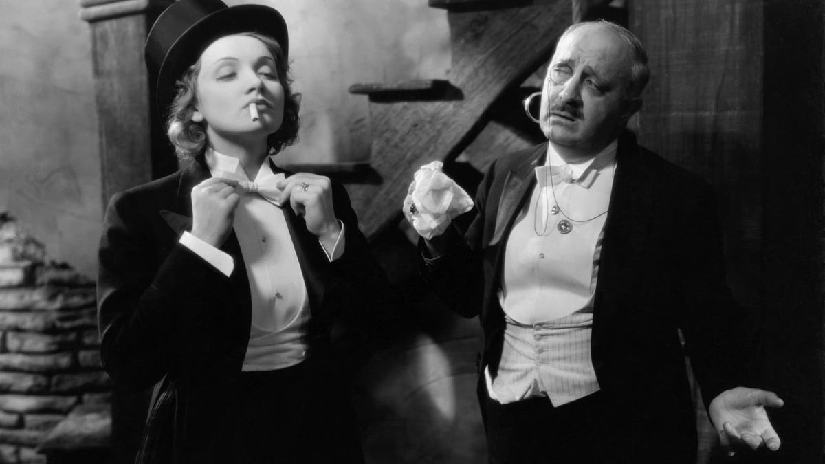 A woman in a tuxedo fixes her clothes while a man looks on in "Morocco"