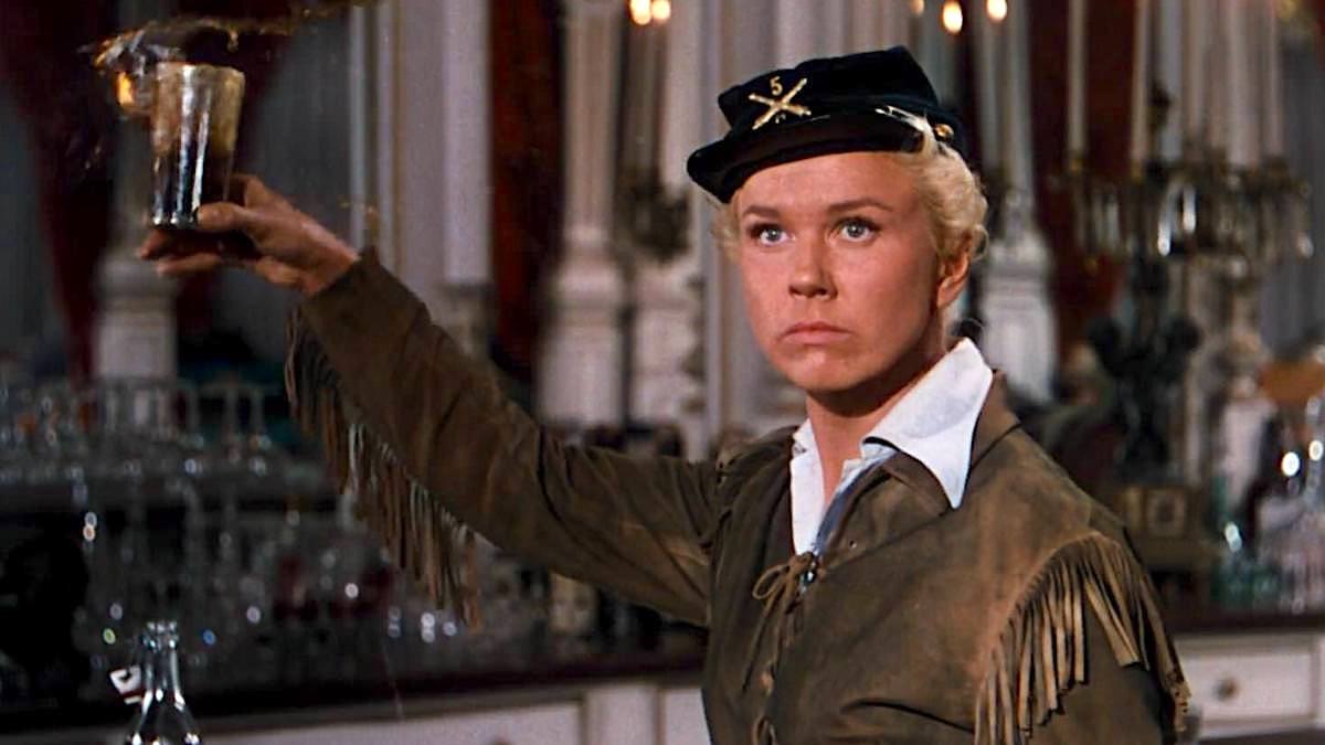 A woman in cowboy clothes holds a glass in a saloon in "Calamity Jane"