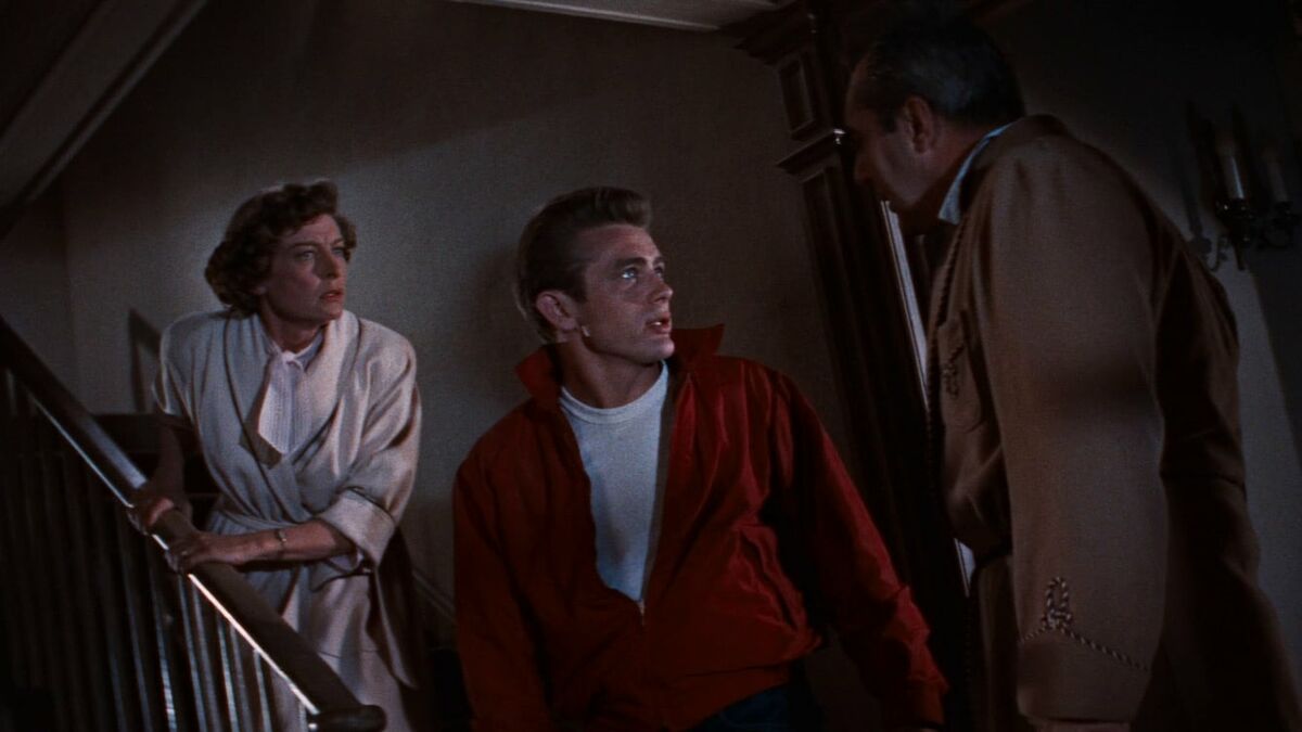 A young man in a red jacket confronts an older man while a woman looks on in "Rebel Without A Cause"