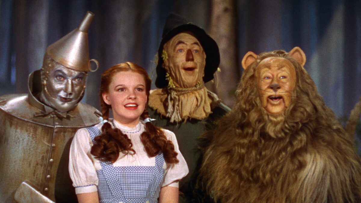 The Lion, Scarecrow, Tin Man and Dorothy stand smiling in "The Wizard of Oz"