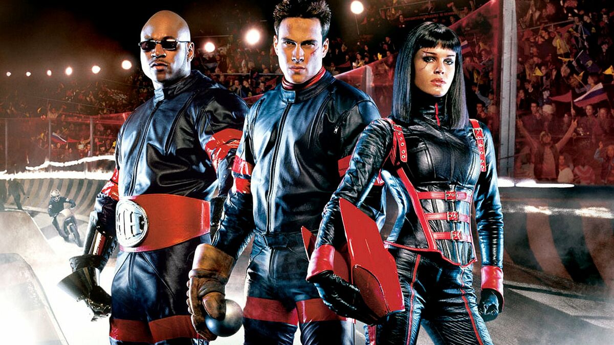 A trio of leather clad riders stand in a stadium in Rollerball