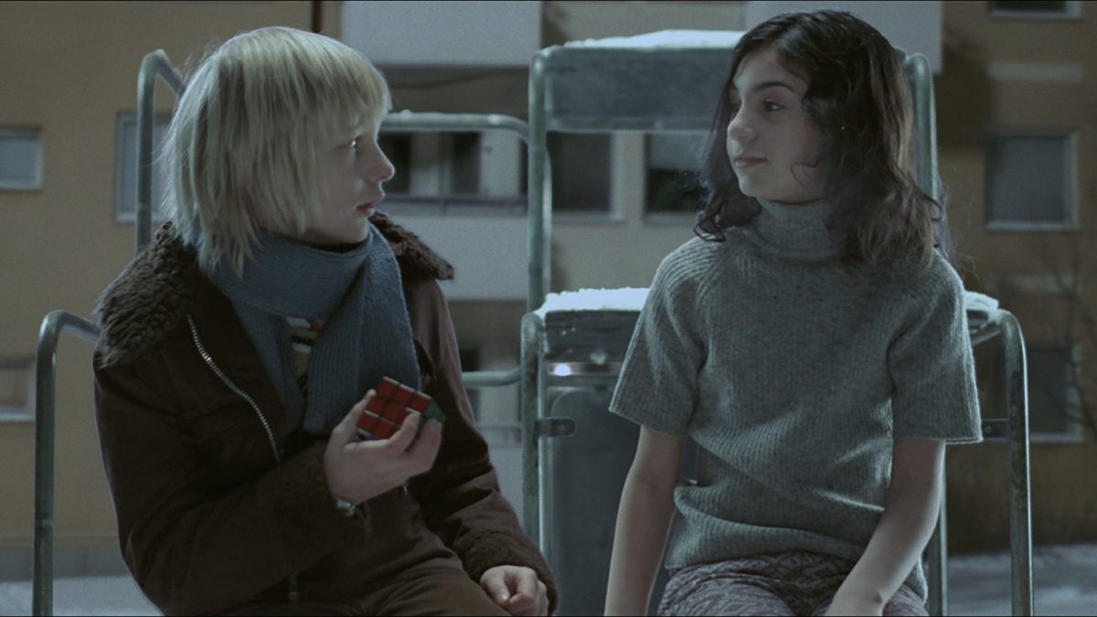 A vampire girl and a blonde boy sit on a playground in Let The Right One In
