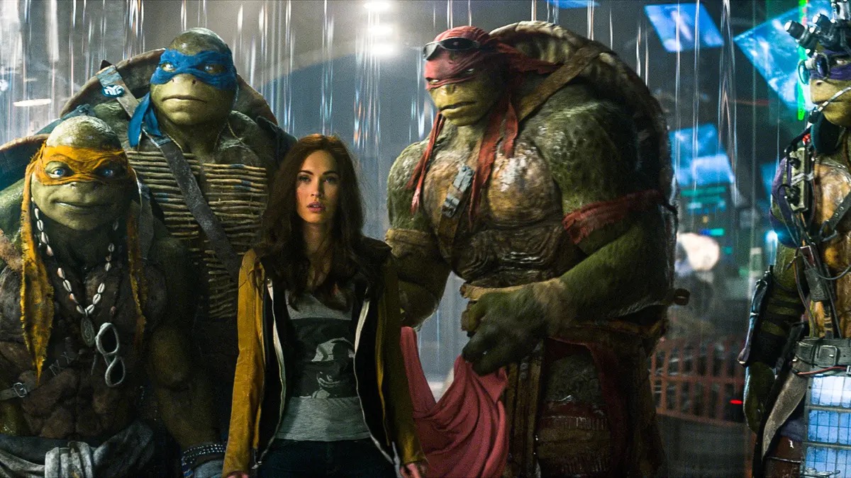 A young woman stands next turtle warriors in Teenage Mutant Ninja Turtles