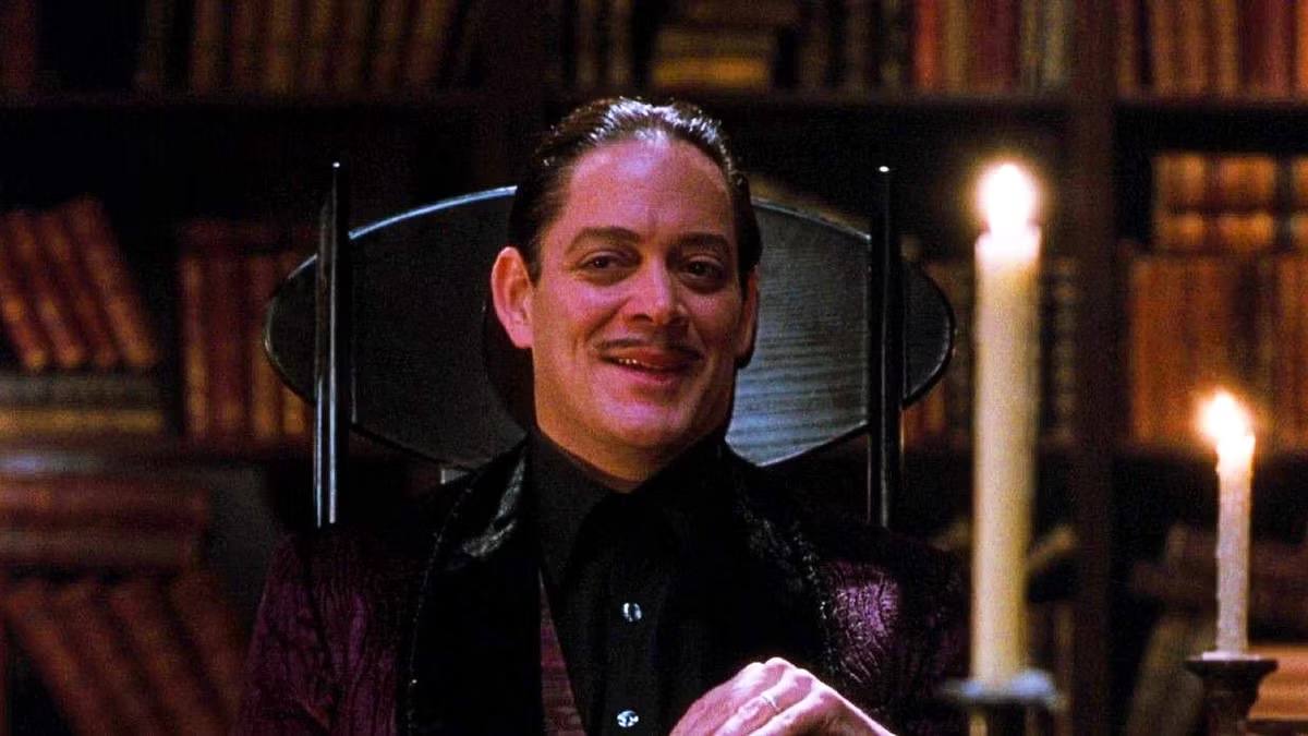 Gomez Addams sits in a study and smiles in The Addams Family
