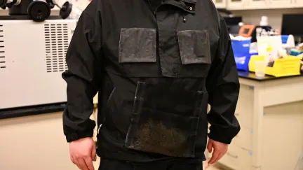 A person is wearing a black jacket with panels; the jacket was created by engineers at The University of Texas at Austin and can harvest water from the atmosphere