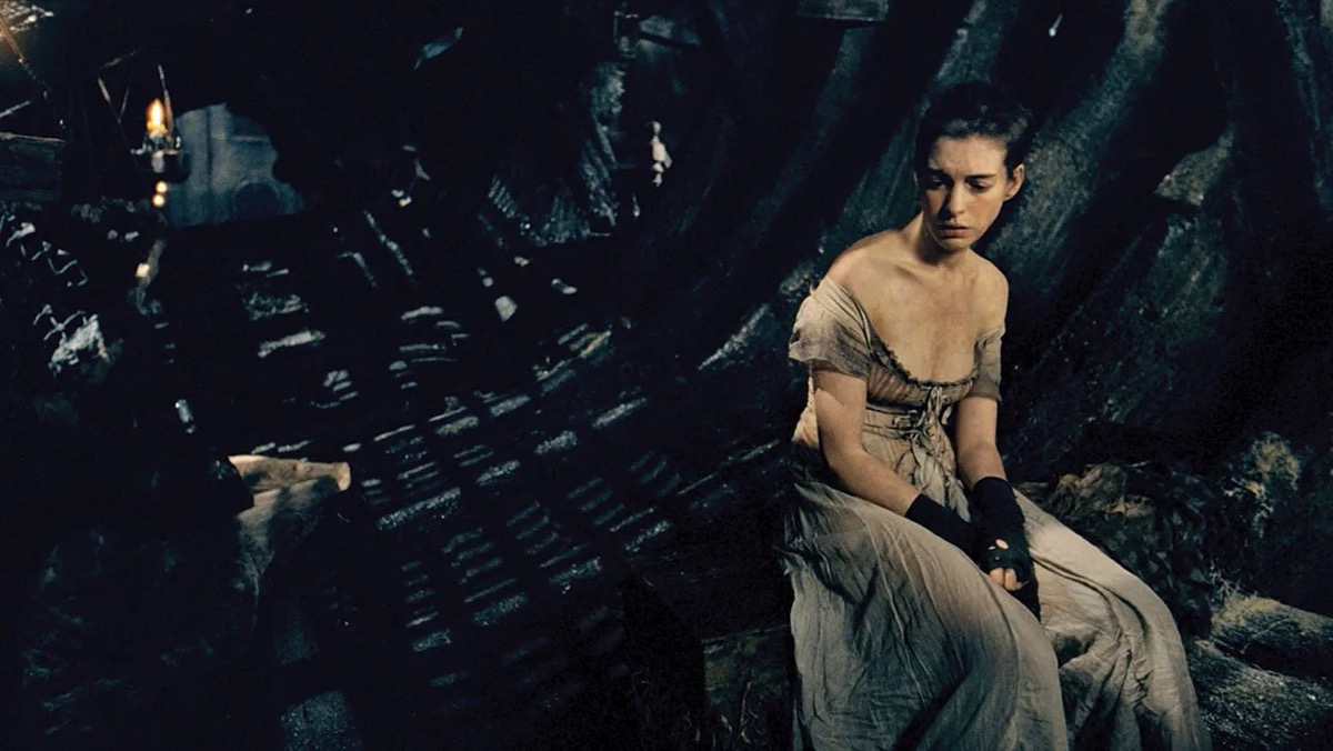 A thin woman sits sadly in a dark room in Les Miserables