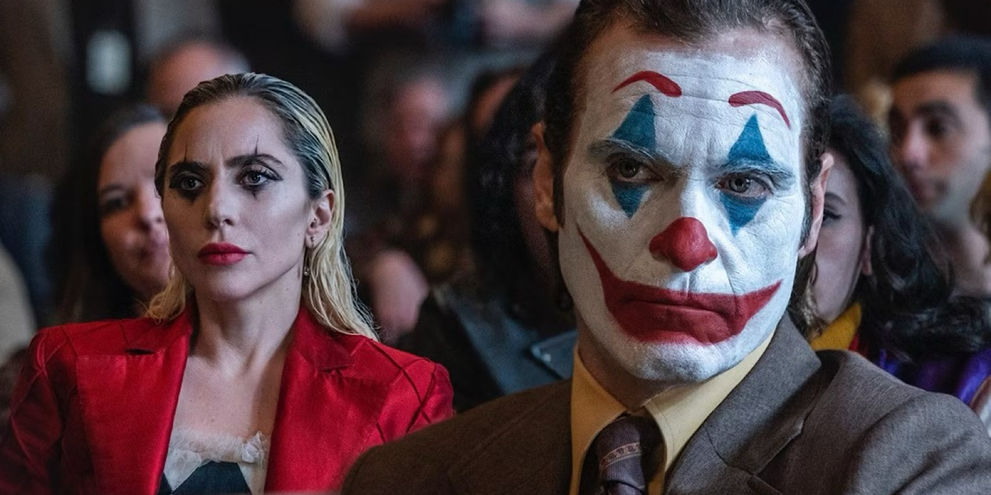 A man with clown make-up sits in front of a woman in a res jacket.