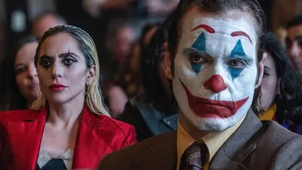A man with clown make-up sits in front of a woman in a res jacket.